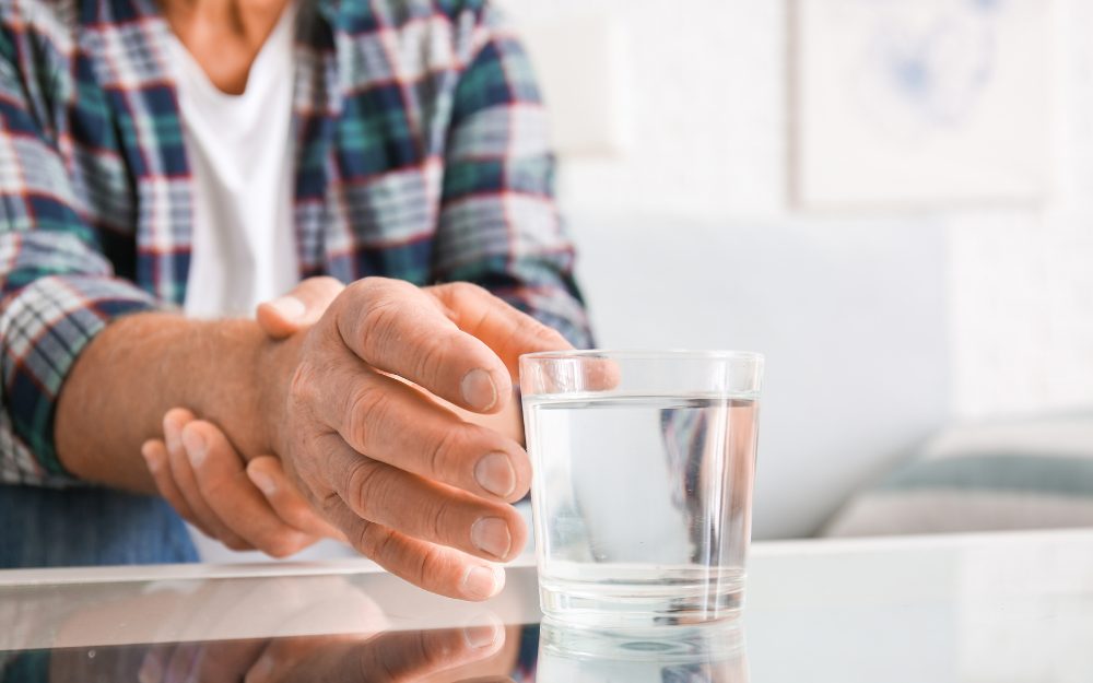 Image of a man holding a shaky cup of water, a potential symptom of Parkinson's disease, indicating tremors in hands.